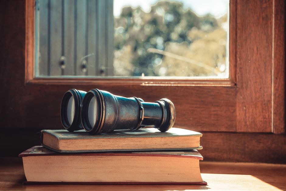 Antique binoculars on stacked books by a window, capturing a vintage and nostalgic feel.